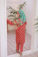 Woman wearing a red and green traditional outfit with a patterned headscarf in a room with plants.