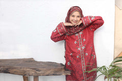 Woman in a red traditional outfit with floral patterns standing indoors.