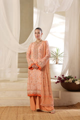 Woman wearing a Orangish peach embroidered traditional outfit in a bright room with sheer curtains.