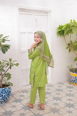 Young girl in a green traditional outfit standing in a room with plants.