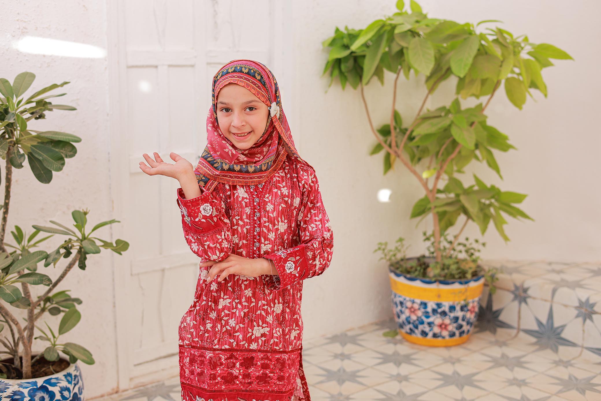 Person in a red outfit standing between two potted plants indoors.