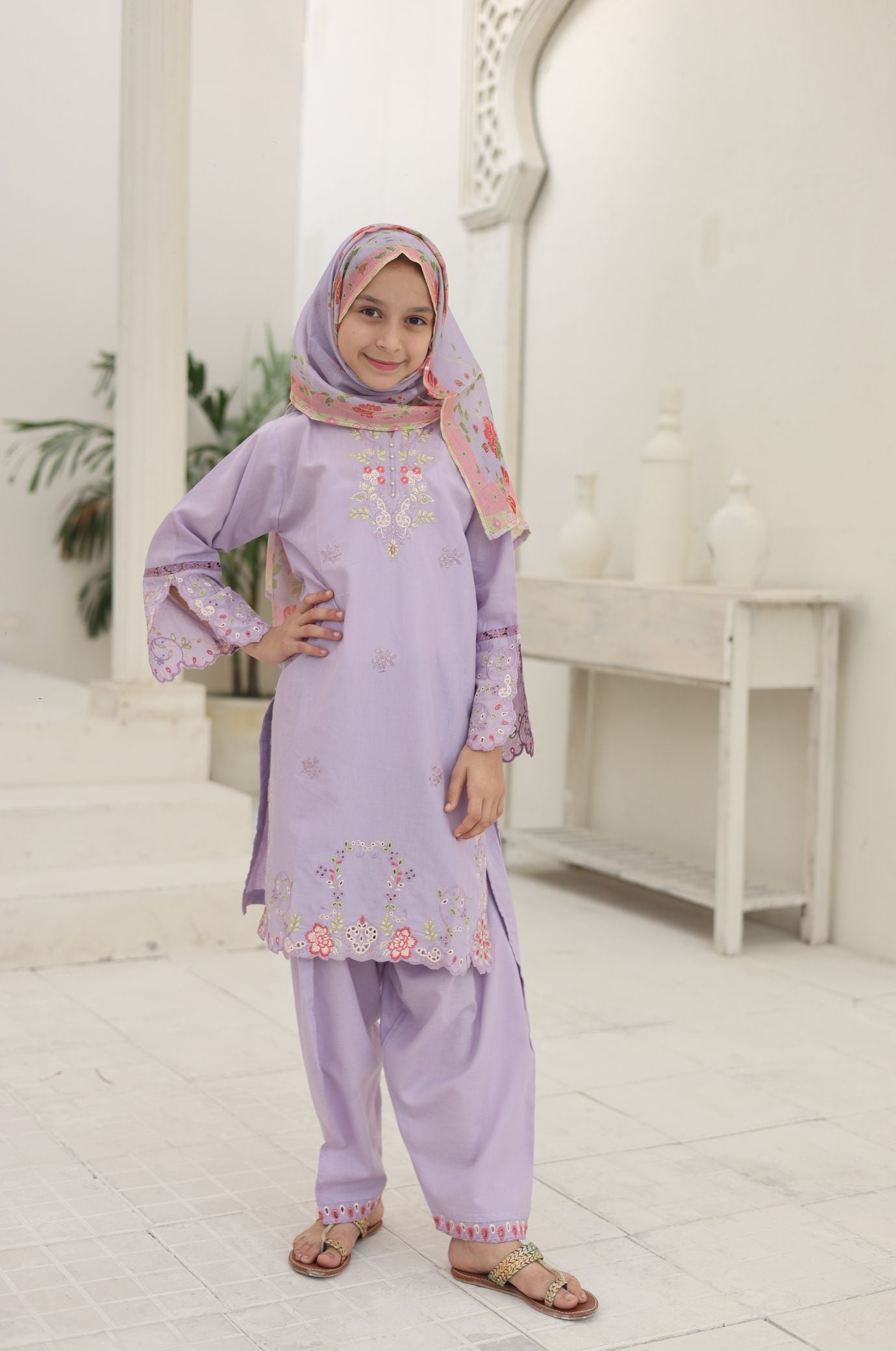 Child wearing a light purple traditional outfit with floral patterns in a bright room.
