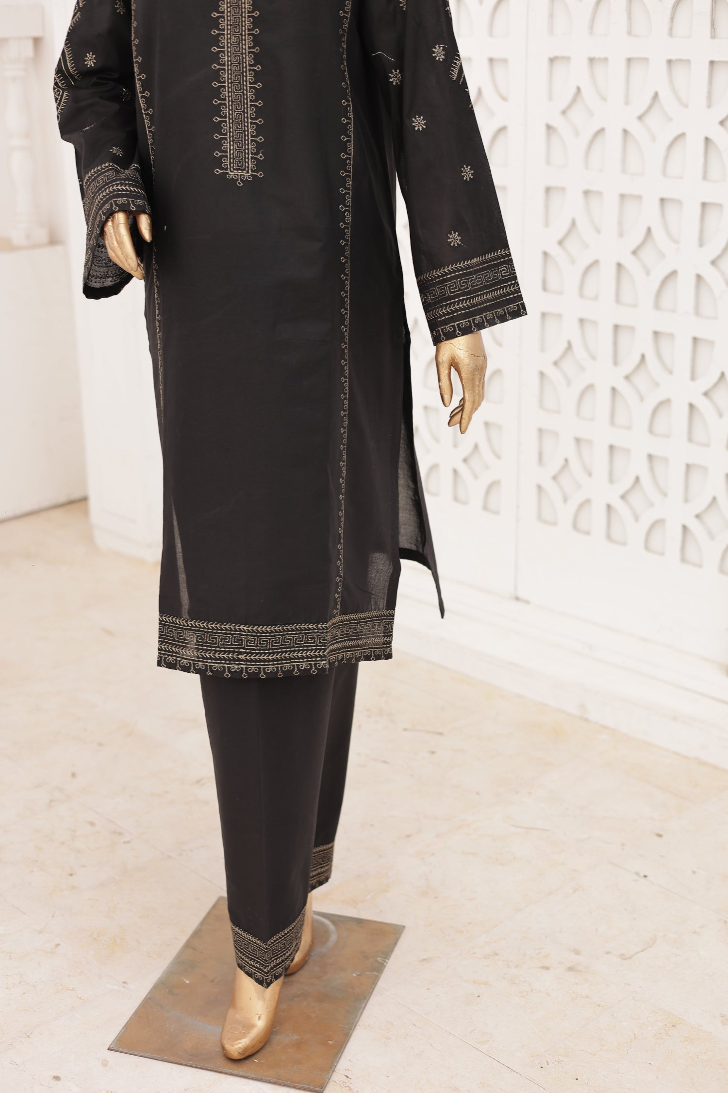 Person wearing black pants with gold accents on a white textured surface