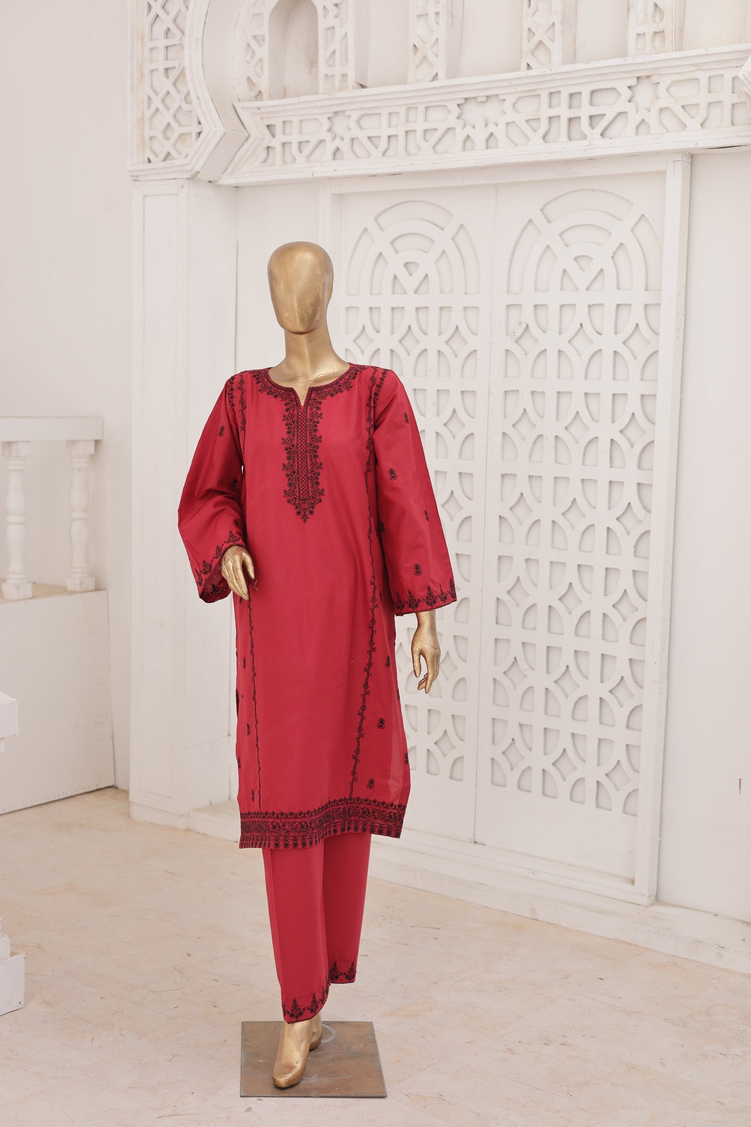Red traditional outfit with black embroidery on a mannequin against a white decorative wall.