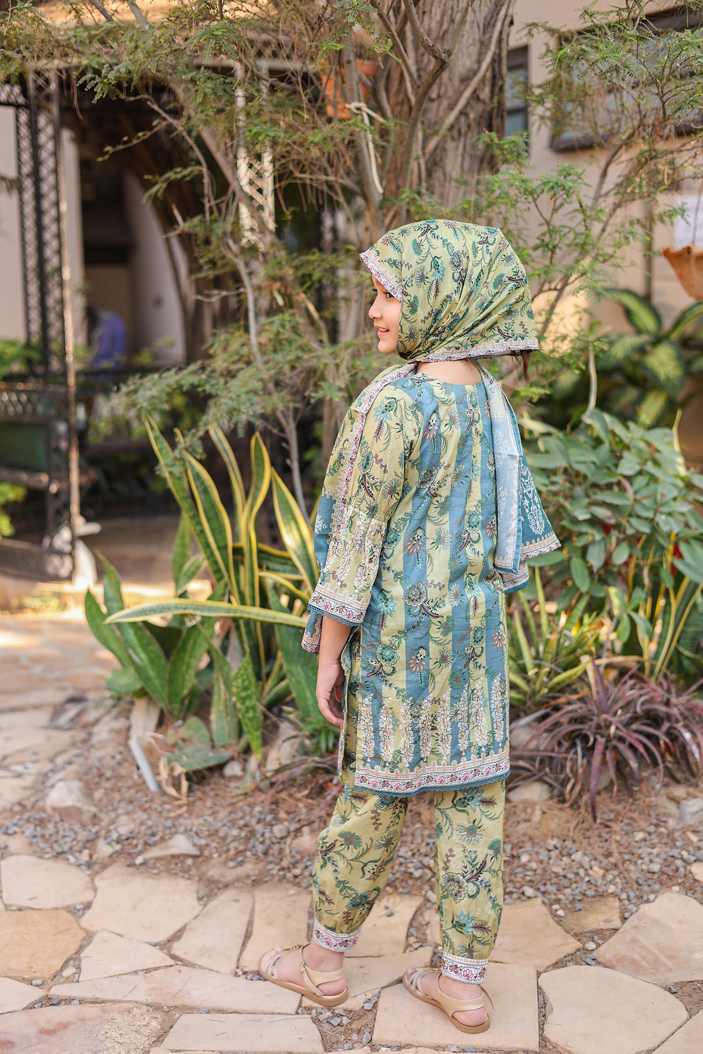 Woman in a green and blue patterned outfit standing outdoors with plants in the background