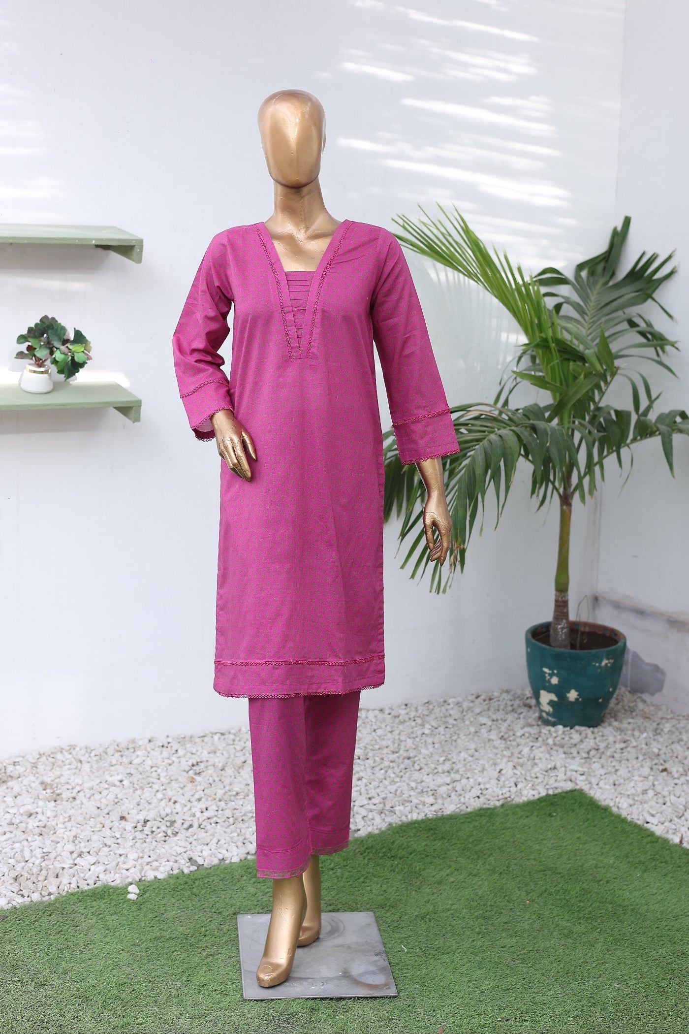 Mannequin wearing a pink outfit with a plant on a white floor.