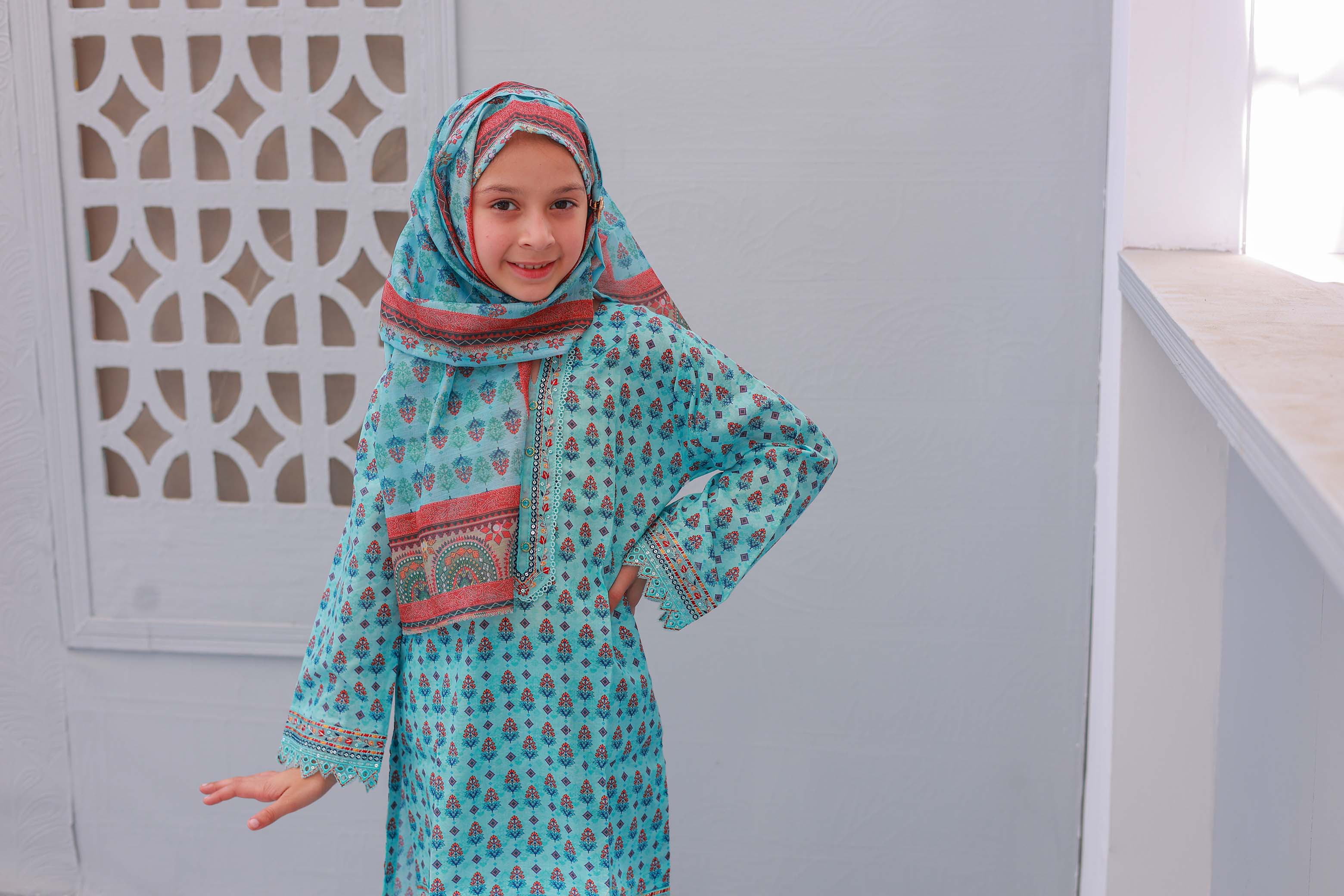 A young girl dressed in a festive embroidered outfit, featuring a sleeved shirt, trousers, and a dupatta.