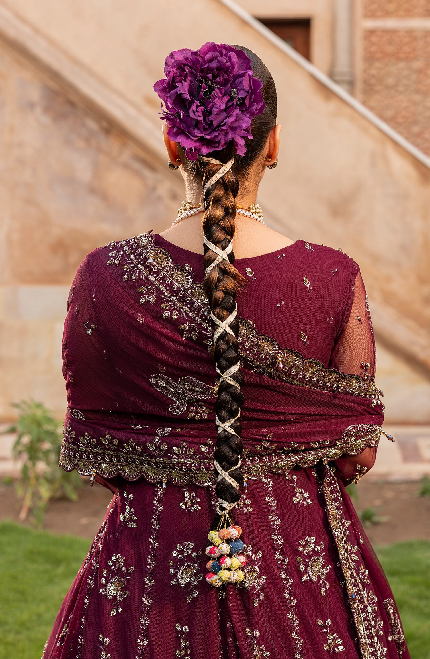 Person wearing a maroon traditional outfit with intricate designs, standing outdoors.