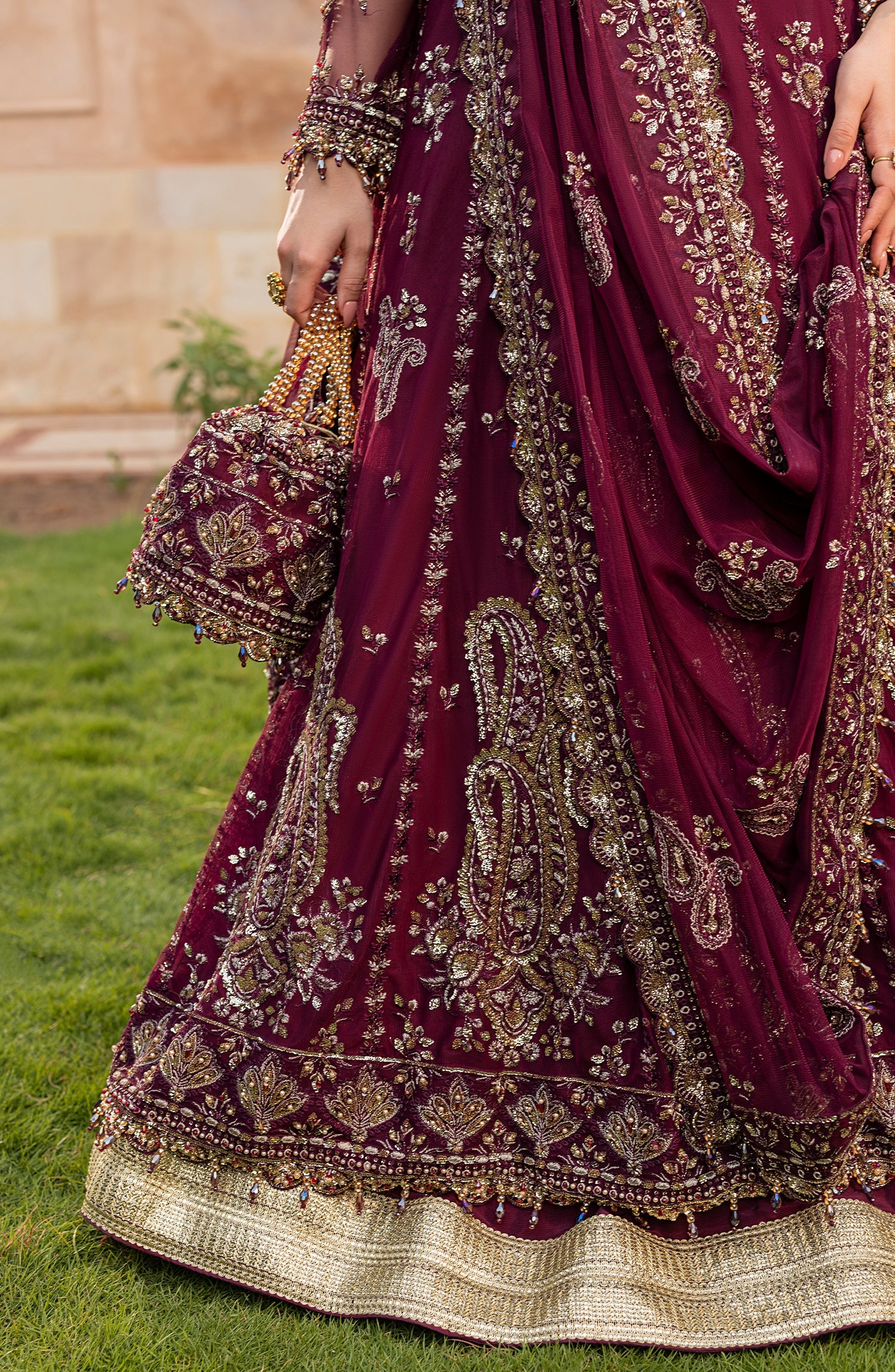 Maroon embroidered traditional outfit with gold details on a grassy background