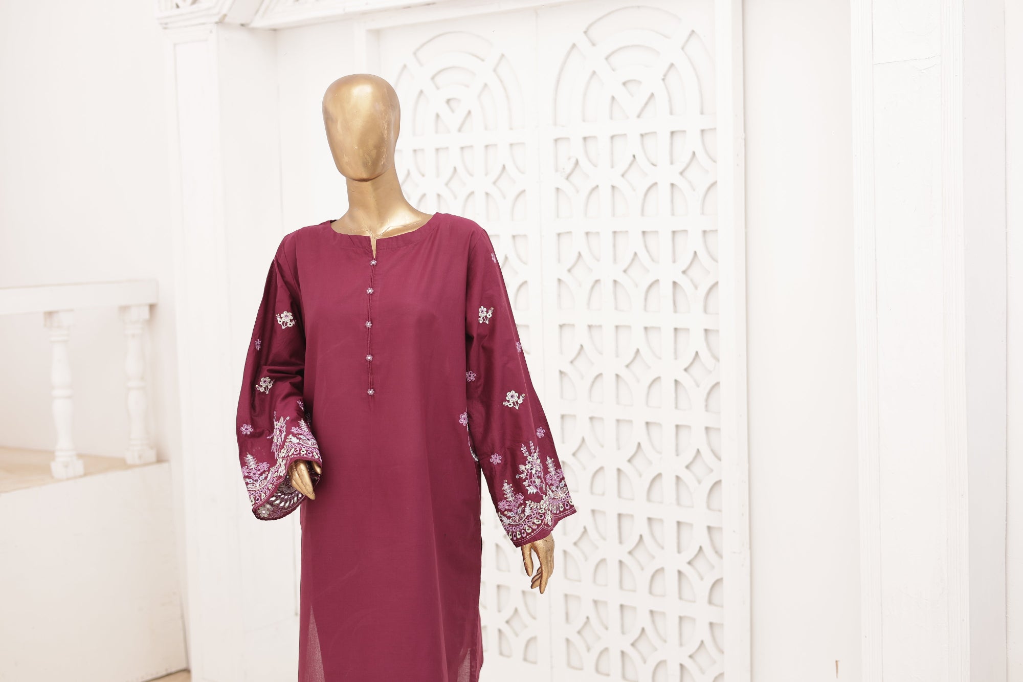 Maroon dress with white patterns on a mannequin against a decorative white wall.