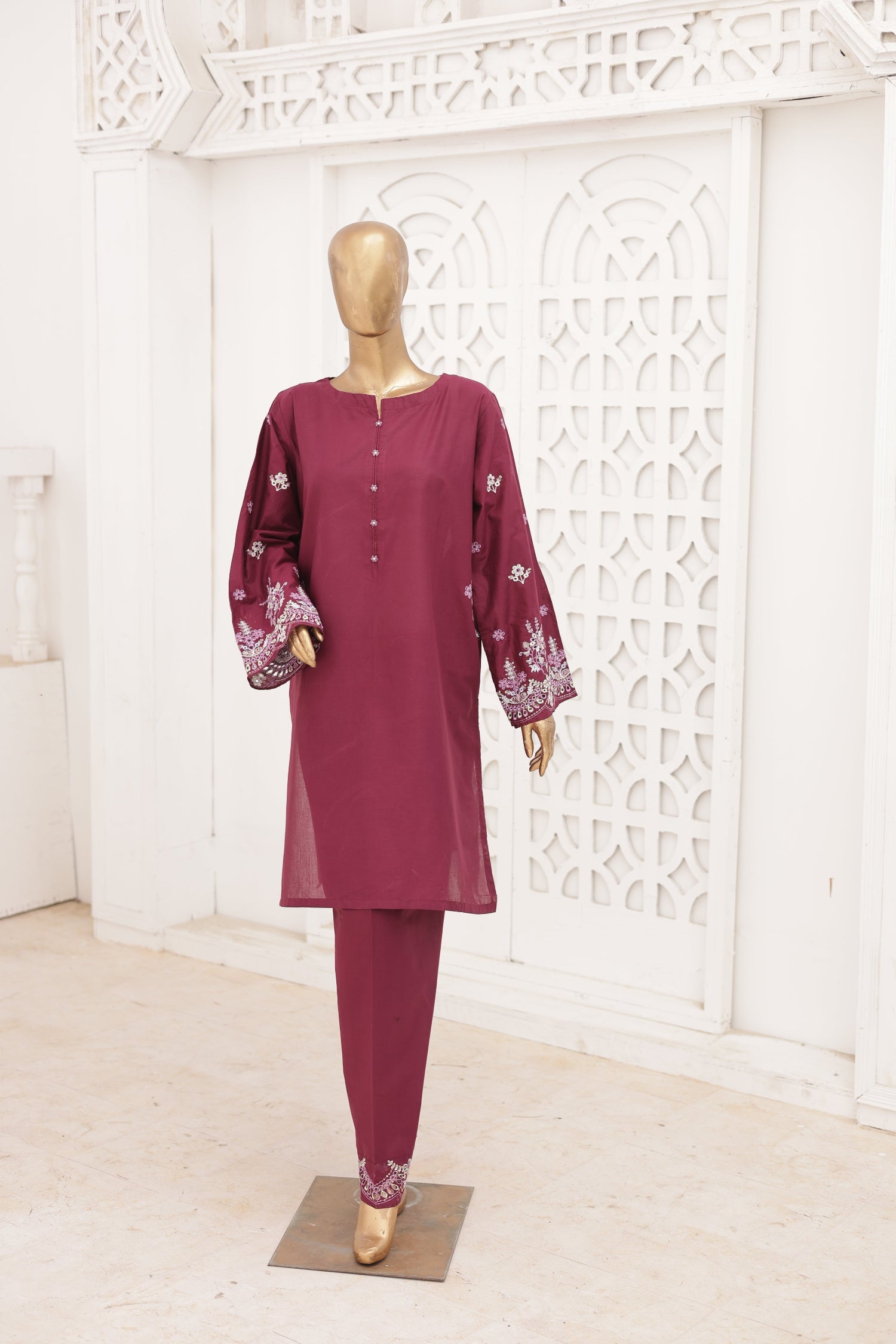 Mannequin wearing a maroon outfit with floral patterns against a white decorative wall.