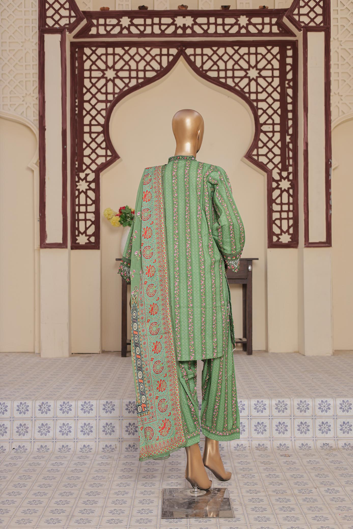 Green embroidered traditional outfit on a mannequin against an ornate wall.