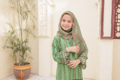 Young girl in a green traditional outfit with a headscarf standing indoors.