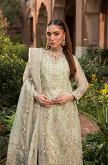 Woman in a light green embroidered traditional outfit standing outdoors with greenery in the background