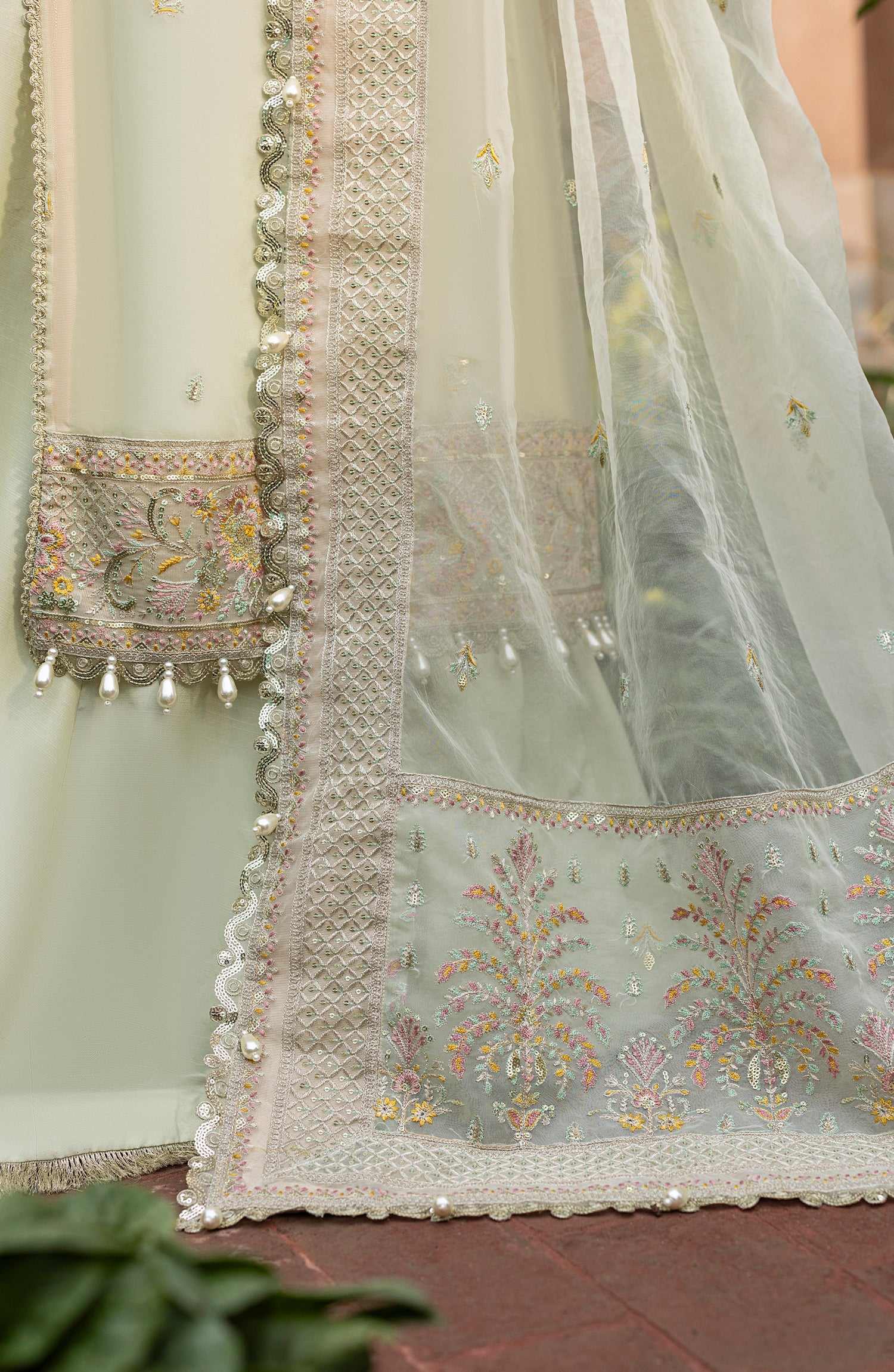 Close-up of a light green embroidered fabric with floral patterns on a red surface.